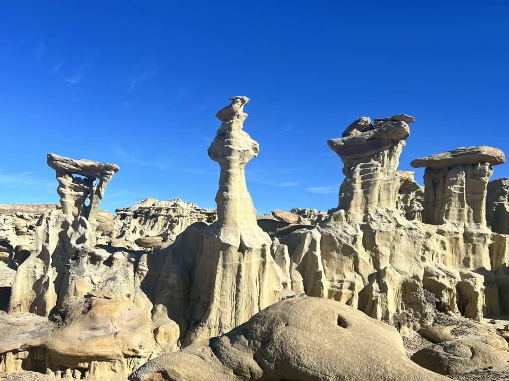 Tall pale stone spires and hoodoos under a bright blue New Mexico sky.