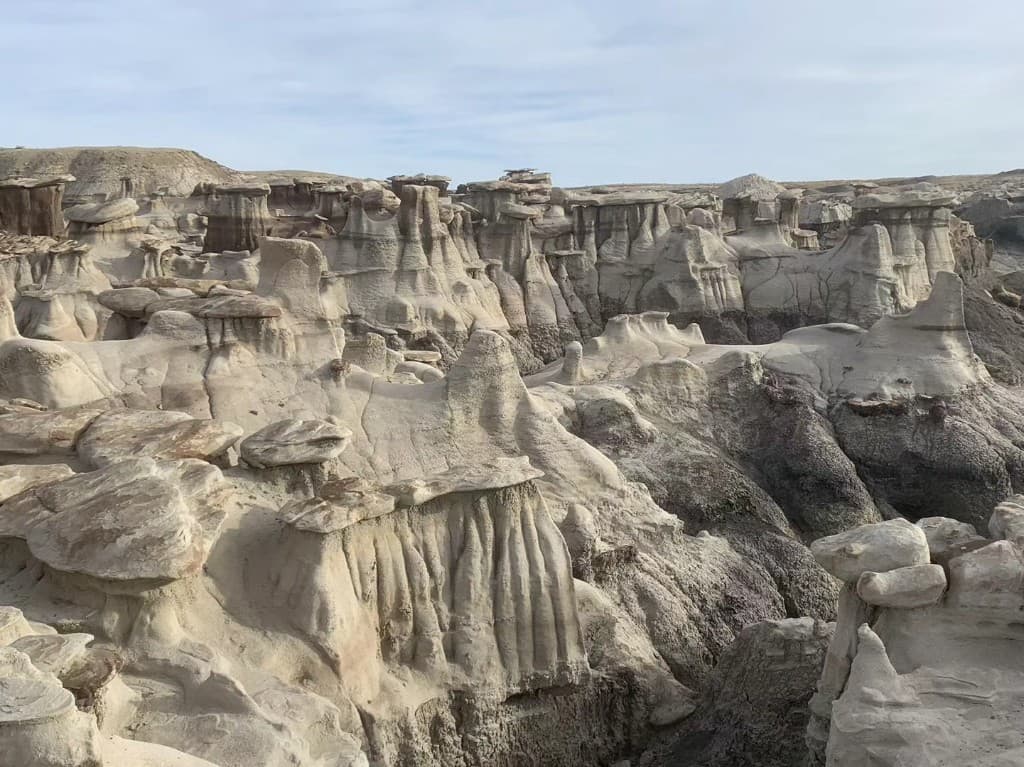 A wide view across weathered hoodoos and badlands formations in muted desert light.