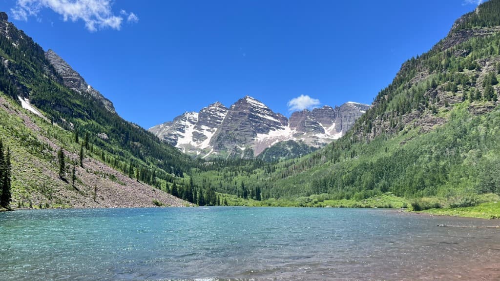 Maroon Bells rising over a blue alpine lake on a clear summer day.